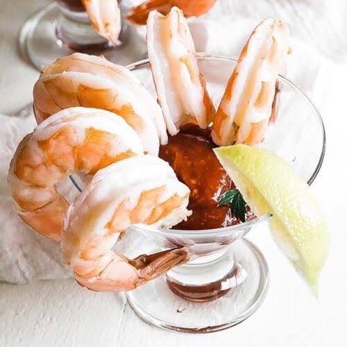 Cooked shrimp cocktail in a stemmed glass with cocktail sauce, lemon wedge, and parsley